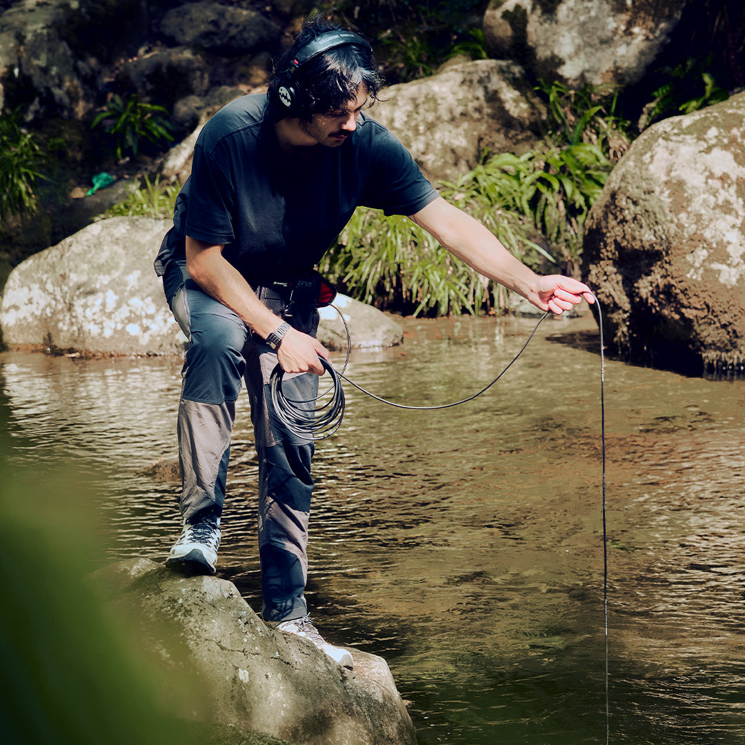 Ollie from Rare Finds standing on a rock by a stream, using a hydrophone, to record water.