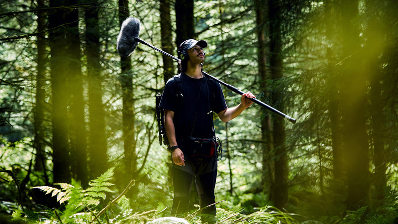 Person holding a microphone in a forest setting